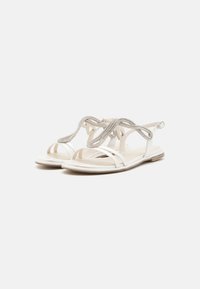 White sandals featuring a sleek design, thin straps, and a textured embellishment on the upper. Soft footbed with a flat sole.