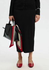 Set cardigan e gonna a coste nere, abbinato a una borsa a tracolla nera decorata con una sciarpa rossa e crema a contrasto, e scarpe basse rosse con punta quadrata.
