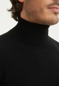 Pull en maille noir à col roulé avec un col côtelé et une texture lisse, au design ajusté, sans logos ni embellissements visibles.