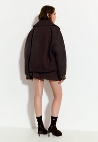 Ruskea ylisuuri villatakki suurella kauluksella, päällä tumman hameen kanssa, yhdistettynä mustiin korkokenkiin ja nilkkasukkiin.