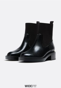 Czarne botki do kostek z błyszczącej skóry, z elastycznymi bocznymi panelami i niskim słupkowym obcasem. Minimalistyczny design bez dodatkowych ozdób.