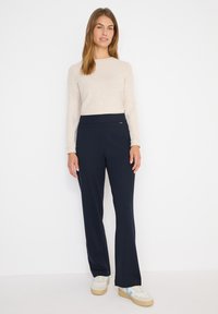 Marineblauwe flared broek van zacht materiaal met een brede tailleband en subtiele voornaaddetails, gecombineerd met een lichtbeige lange mouw top.