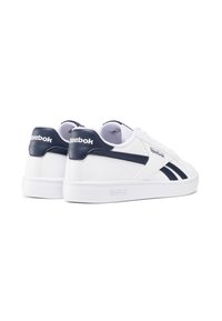 Baskets Reebok blanches avec une finition en cuir lisse, des accents bleu marine, un design bas et une semelle en caoutchouc texturée avec un logo.