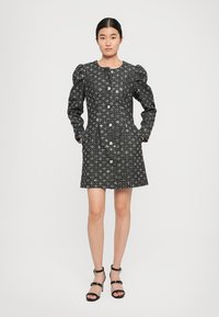 Black dress with puffed sleeves, button front, and pockets. Fabric features a subtle star pattern. Model wears strappy black sandals.