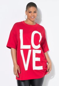 T-shirt rossa oversize in cotone, con grandi lettere bianche che scrivono "LOVE" sulla parte anteriore. Maniche corte e scollatura rotonda.
