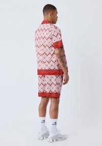 Conjunto de camisa de manga corta y pantalones cortos de patrón rojo y blanco con ribete rojo contrastante. Los pantalones cortos son hasta la rodilla y la tela parece suave.