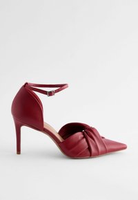 Sandale à talons hauts en cuir rouge avec un bout pointu, un détail en nœud à l'avant et une bride à la cheville avec une boucle en argent.