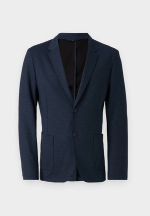 Sarkana zila žakete izgatavota no teksturēta auduma, ar ieliektu apkakli, divām pogām un divām priekšējām kabatām. Priekšā atvērta.