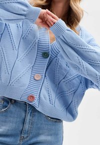 Ljusblå stickad kofta med texturerat mönster, ribbade muddar och tre knappar i grönt, rosa och brunt.