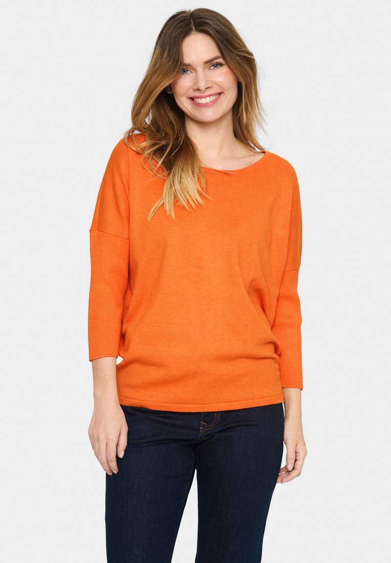 Strikket orange sweater med tekstur, bred halsudskæring og trekvartærmer, parret med mørkeblå jeans. Glat og afslappet pasform.