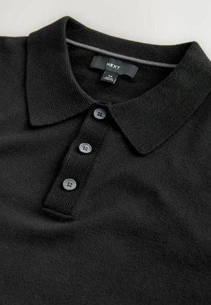 Tricou polo negru cu guler, trei nasturi întunecați și material texturat. Etichetă cu inscripția "NEXT" și informații despre dimensiune.