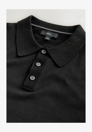 Polo noir avec un col, trois boutons foncés et un tissu texturé. Étiquette portant la mention "NEXT" avec des informations de taille.