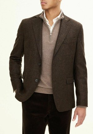Braun gestreifter Blazer mit zwei Knöpfen, getragen über einem hellbraunen Pullover mit Reißverschlusskragen. Besondere Merkmale sind der schlanke Schnitt und der strukturierte Stoff.