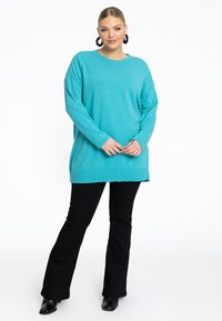 Turquoise oversized trui van een zachte breimateriaal, met lange mouwen, geribbelde manchetten en een zij-split zoom, gecombineerd met zwarte flare broeken.