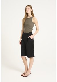 Shorts neri su misura con una vestibilità rilassata, dotati di tasche laterali, abbinati a una canotta aderente color oliva realizzata in tessuto a coste.