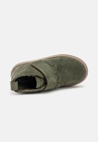 Stivaletto in suede verde khaki con strap in velcro, punta tonda, finitura testurizzata e fodera morbida. Suola piatta in gomma con asola per un facile indossamento.