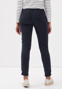 Pantalones azul marino de corte ajustado con textura suave, dos bolsillos traseros y puños doblados. Combinados con zapatos espadrilles de color claro.