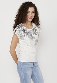 T-shirt blanc à manches courtes avec des motifs de feuilles en métal argenté. Tissu doux avec un col rond classique et une coupe ajustée.