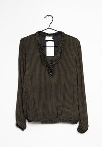 Blouse noire avec des pois dorés, décolleté froncé et un détail de bouton. Manches longues avec ourlet froncé, suspendue à un crochet noir.