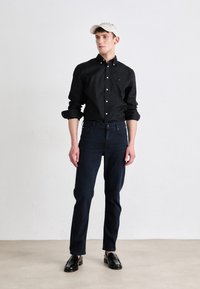 Black button-up shirt, dark denim jeans, beige cap, and black loafers. Slim fit, smooth fabric, and classic design.