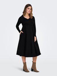 Czarna sukienka z długim rękawem, dekoltem w serek, marszczonym stanem oraz kieszeniami. Zwiewna spódnica o gładkiej fakturze, uzupełniona jasnobrązowymi botkami za kostkę.