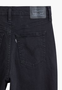 Bakifrån av svarta Levi's-jeans som visar den högra bakfickan med signaturens bågformade sömnad och grå läderpatch från Levi Strauss & Co.