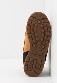 Botas de ante marrón con detalles en negro, que presentan una suela de goma resistente, un diseño de banda de rodadura pronunciado y un logotipo de árbol en la suela.