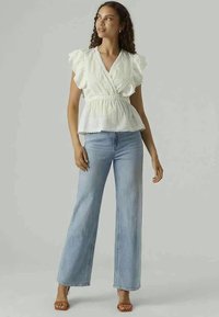 Top peplum branco com mangas em babados, usado com jeans de perna larga azul claro. O top apresenta riscas verticais e uma cintura ajustada.