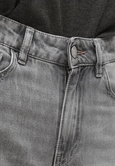 Jean en denim gris avec une fermeture à boutons, des passants pour ceinture et une légère texture délavée. Gros plan sur la taille et la zone de la poche avant.