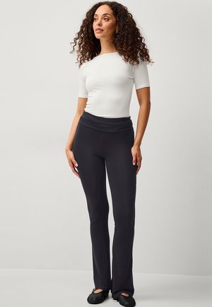 Schwarze, ausgestellte Yogahosen mit hohem Bund und glatter Textur, kombiniert mit einem eng anliegenden, weißen T-Shirt mit kurzen Ärmeln.