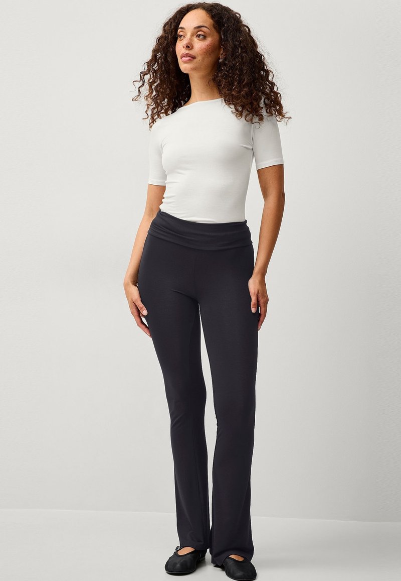 Pantaloni yoga neri svasati con vita alta e texture liscia, abbinati a una maglietta fitted bianca a maniche corte.