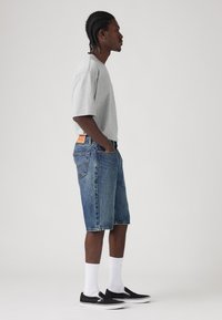 Gray short-sleeve shirt, blue denim shorts, and black slip-on shoes with white soles. Shorts have a faded texture and five-pocket design.