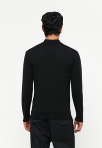 Zwarte gebreide trui met lange mouwen en een polokraag, met een aansluitend ontwerp en geribbelde manchetten en zoom. Soepele textuur, minimale details.