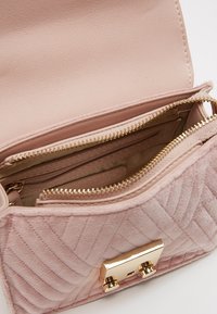 Blushrosa kviltad handväska i texturerat material, med ett guldspänne och flera fickor med dragkedjor för organiserad förvaring.