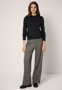 Maglione scuro in misto lana con scollo a girocollo, abbinato a pantaloni a gamba larga a vita alta grigi a quadri e calzature nere.