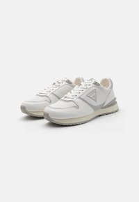 Zapatillas deportivas blancas de cuero liso, con acentos en gris claro, puntera redonda, cordones planos y una suela de goma texturizada con un detalle de logo.