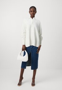 Camicia bianca a maniche lunghe con bottoni e vestibilità su misura, abbinata a una gonna di jeans scura con spacco frontale e una borsa a tracolla in raso bianco.