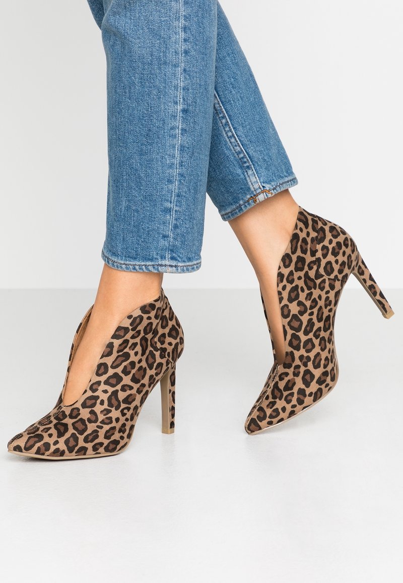 Chaussures à talons hauts imprimé léopard avec bout pointu et côtés ouverts, fabriquées en tissu doux. Talon aigu notable. Portées avec un jean retroussé.