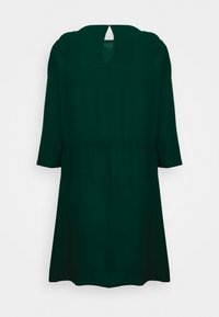 Vestido verde escuro com decote arredondado, mangas a três quartos e abertura em gota nas costas. Tecido fluido, cintura ajustada e forma em A.
