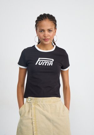 Sort kortærmet t-shirt med hvid krave og manchetter, prydet med et stort hvidt "PUMA" logo på forsiden. Båret med en beige nederdel.