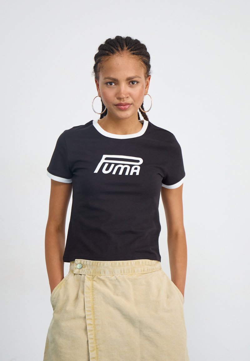 Tricou scurt negru cu mânecă scurtă, la guler și mansete albe, având un mare logo alb "PUMA" pe față. Purtați cu o fustă bej.