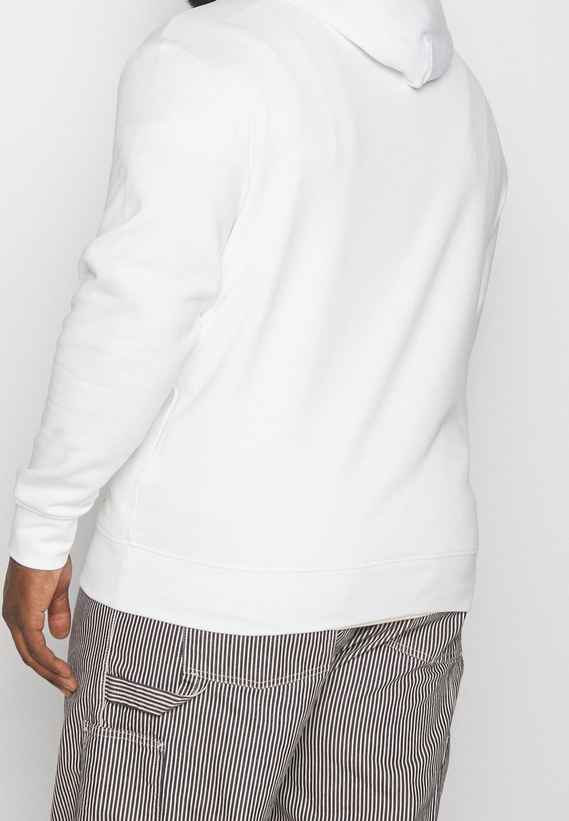 Sudadera blanca hecha de tela suave, con mangas largas y capucha con cordón, combinada con pantalones cargo a rayas.