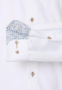 Weißes Hemd mit blauen Muster an den Manschetten. Aus glattem Stoff, sichtbaren Nähten und zwei goldenen Knöpfen an den Manschetten und der Knopfleiste.