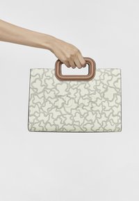 Biała torebka z teksturowanym szarym wzorem, brązowym uchwytem, prostokątnym kształtem i minimalistycznym designem, trzymana w dłoni na jednolitym tle.