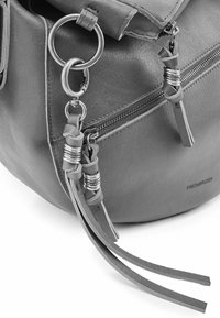 Sac en cuir gris avec une surface texturée, équipé de ferrures métalliques, de glands décoratifs et d'une poche zippée sur le côté.