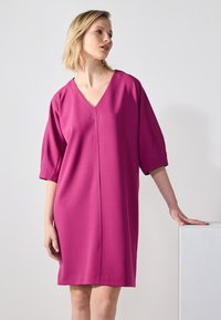 Fukszia ruha V-nyakkal, rövid ujjal és egyenes fazonnal. Simább anyagból készült, középső varrással. Minimalista dizájn.