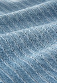 La tela de mezclilla azul claro presenta un sutil patrón de rayas verticales, con líneas definidas y una textura suave.