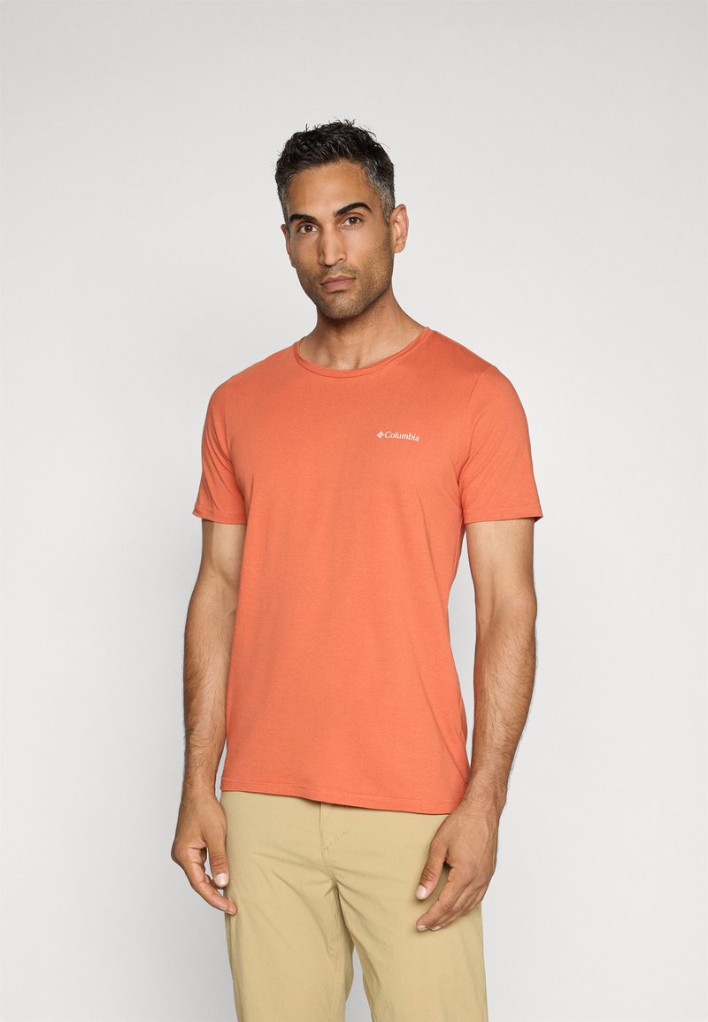 Kurzärmliges, Rundhals-T-Shirt in Korallenorange, aus weichem Stoff mit einem kleinen weißen Logo auf der linken Brust. Schlichtes und figurbetontes Design.