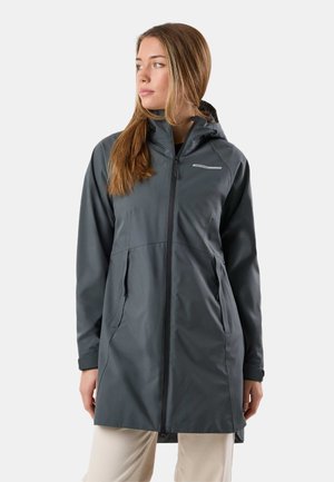 Femme portant une longue veste imperméable à capuche de couleur gris foncé avec une fermeture éclair à l'avant et des poches latérales zippées, regardant vers sa gauche.
