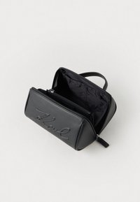 Must musta nahk-kott, millel on pealmine tõmblukk ja tekstuuriga logo. Sellel on avar sisekott, mis on kaetud tumeda kangaga, sisaldades lisaks ka tõmblukuga taskut.